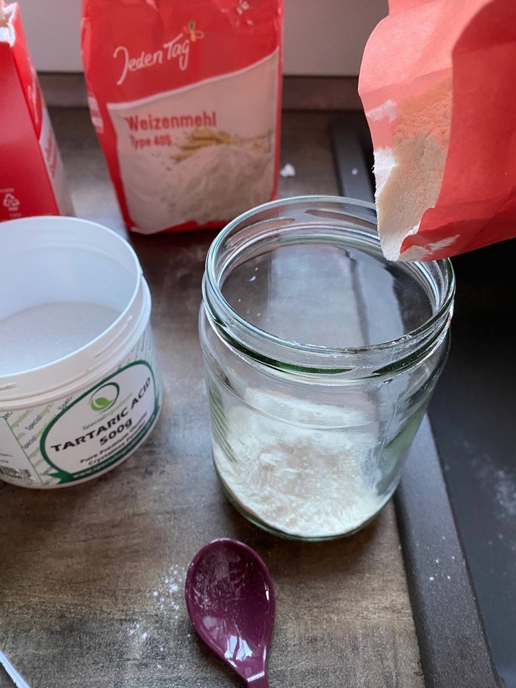 Mehl wird aus der Packung in ein Schraubglas gefüllt.