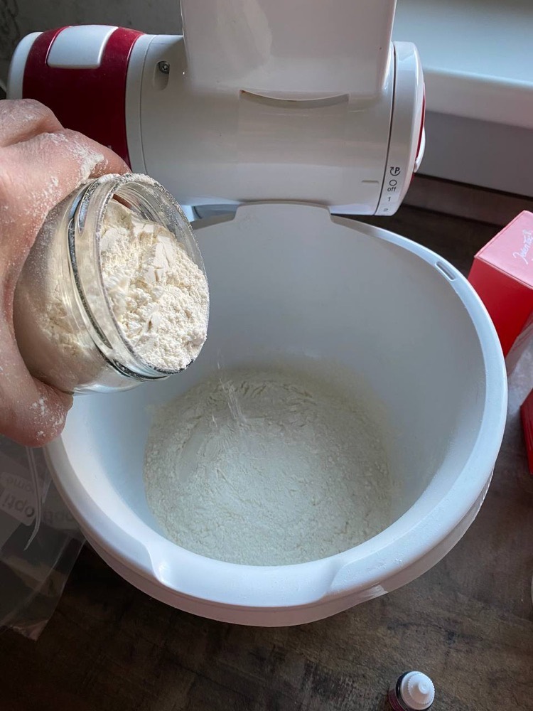 Das Mehl wird aus dem Glas in die weiße Rührschüssel der Küchenmaschine geschüttet.